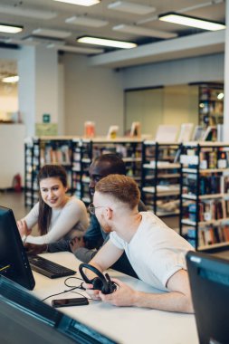 Modern kütüphanede masa başında otururken kulaklıkla bilgisayar okuyan ve gezinen çok ırklı çok ırklı gençler.