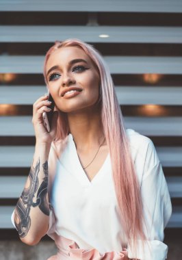 Milenyum kadını, renkli pembe saçlı, uygulamayla akıllı telefon görüşmesinden zevk alan, elinde büyük moda dövmesi olan beyaz yeniyetme bir kız, telefon etmek için uluslararası dolaşımı kullanıyor.