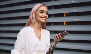 Milenyum yeniyetme hippi kız elinde renkli ders kitapları ve sosyal ağlardaki içerik yayınından şehrin sokaklarında gülümsüyor. Pembe saçlı genç kız cep telefonu cihazını açık havada kullanıyor.