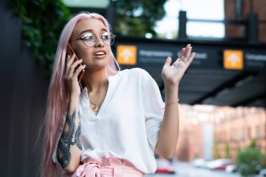 Görme düzeltmesi için optik gözlüklü çekici bir kadın akıllı telefon cihazıyla telefon ederken en iyi arkadaşıyla şok edici bilgiyi tartışıyor. Gezgin, genç ve güzel bir hippi kız.