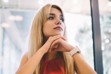 Şık, genç bir kadın, sarı saçlı. Masada oturmuş modern kafenin camına yaslanırken başka tarafa bakıyor ve düşünüyor.