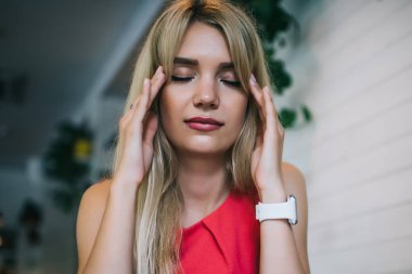 Kırmızı elbiseli, yorgun bir bayan öğrenci masadaki kitap ve sınava hazırlanırken tapınakları ovuyor ve konsantre oluyor.