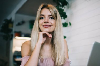 Akıllı saat takan mutlu modern kız öğrenci laptop ve akıllı telefonla masada oturuyor ve kafede boş zaman geçirip internette gezinirken kameraya bakıyor.