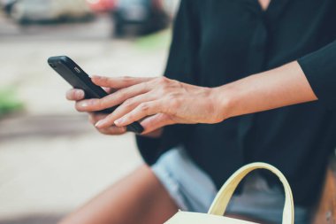 Milenyum yeniyetme kızın akıllı telefon klavyesiyle metin içeriği yazarken görüntüsü kesildi. Şehir bankında dinlenirken ve internet bağlantısı kurarken, kadın blogcu yayın yapıyor.