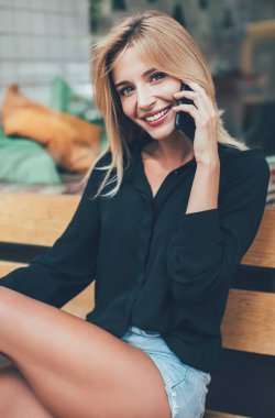 Sıradan giyinmiş neşeli yeniyetme kız portresi uluslararası dostça sohbetler sırasında cep telefonu uygulaması üzerinden kameraya gülümsüyor, pozitif milenyum kadını 20 'li yaşlarda şehir bankında dinleniyor.