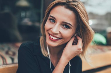 Boş bir yaşam tarzı ve meloman insanlar konsepti. Yüzünde samimi bir gülümseme olan, müzik dinlemek için elektronik kulaklık kullanan beyaz bir kızın portresini yakından çek.