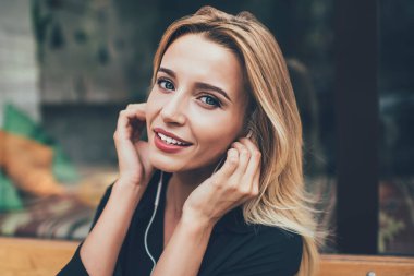 Giyilebilir elektronik kulaklıklı çekici bir kadın melodinin portresi. Çalma listesindeki favori müziği dinliyor ve boş zamanlarında kameraya bakıyor. Güzel bir kadın müzik kaydından zevk alıyor.