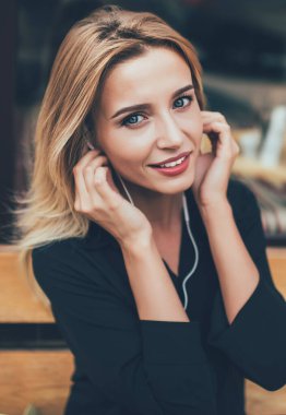 Elektronik kulaklıkla müzik dinlemek için zaman harcayan genç bir kadının portresini kapat. Açık havada eğlenmenin tadını çıkar. Siyah gömlekli çekici bir kadın kameraya bakıyor ve müzik şarkısını dinliyor.