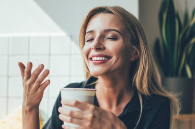 Kafeteryadaki molada elinde bir fincan sıcak kahveyle gülümseyen ve onu koklayan güzel beyaz bir kız. Kafeteryada kafein kokusundan zevk alan pozitif bir kadın.