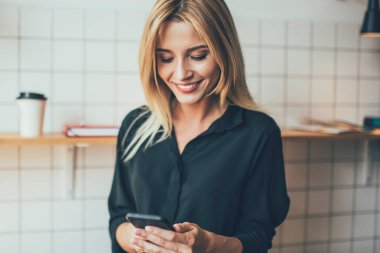 Gündelik giyinmiş neşeli beyaz kız akıllı telefon cihazıyla telefon ediyor, internet bağlantısını kullanıyor, takipçilerden e-posta alırken gülümseyen mutlu kadın blogcu