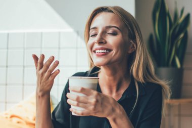 Kafeteryadaki molada elinde bir fincan sıcak kahveyle gülümseyen ve onu koklayan güzel beyaz bir kız. Kafeteryada kafein kokusundan zevk alan pozitif bir kadın.