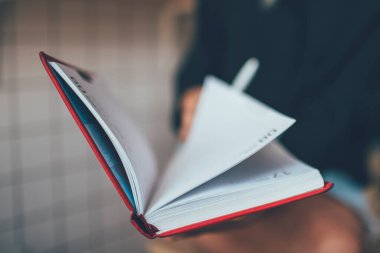 Zaman yönetimi planlamak için kırmızı kağıt ders kitabına seçici odaklanma, eğitim için not defteri kullanan ve ders çalışması ve bilgi notları yazan kız öğrencinin kırpılmış görüntüsü