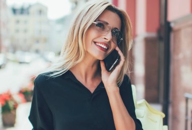 Hoş gülüşü olan neşeli bir kadın cep telefonuyla dostça sohbet ederken kendini iyi hissediyor. Seyahatler sırasında şehir ortamında günlük kıyafetlerini giymiş mutlu bir beyaz kadın.