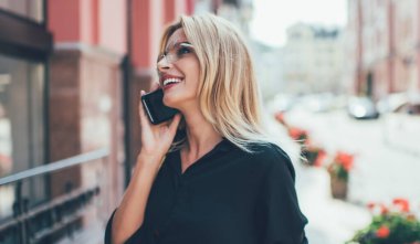 Modern cep telefonuyla en iyi arkadaşına telefon ederken gülen neşeli yeniyetme kızın yandan görünüşü. Yaz tatilinden kalma izlenimleri paylaştığı için. Akıllı telefon uygulaması kullanarak güneş gözlüklü mutlu kadın turist.