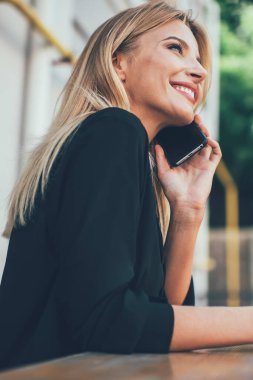 Heyecanlı gülümseyen kadın, boş zamanlarında cep telefonundan iyi haberler duymaktan mutlu, duygusal beyaz kız cep telefonuyla en iyi arkadaşına başvuru yoluyla telefon ediyor.