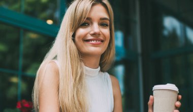 Sıcak içecek gülümseyen ve kamera görünümlü güzel genç kadın Smartphone tarama ve açık kafede masada oturan iken