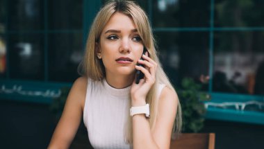 Güzel genç kadın düşünme ve uzak görünümlü cep telefonu ve açık kafede masada not defterinde yazma konuşurken