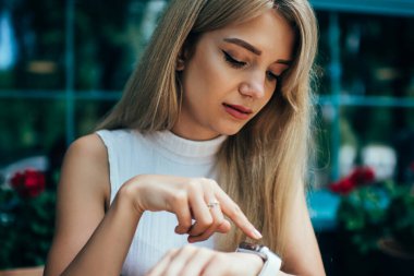 Şehir sokakta açık kafede masada otururken sarı saçlı güzel genç kadın şık SmartWatch ekranında bakıyor ve bildirimleri kontrol