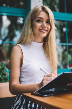 Masada otururken ve açık kafede panoya notlar yaparken güzel genç kadın gülümseyen ve kamera bakıyor