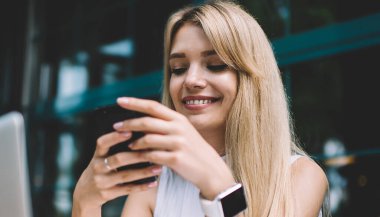 Güzel genç kadın gülümseyen ve şehir sokakta rahat açık kafede otururken ve serbest iş yaparken Smartphone tarama