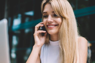 Açık kafede serbest iş yaparken akıllı telefon ve tarama modern laptop konuşurken büyüleyici gülümseme ile güzel genç kadın