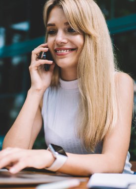 Açık kafede serbest iş yaparken akıllı telefon ve tarama modern laptop konuşurken büyüleyici gülümseme ile güzel genç kadın