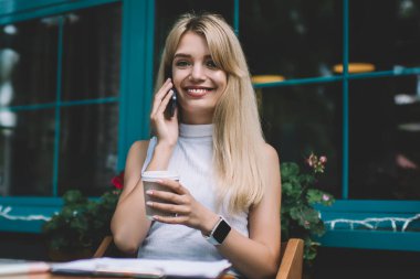Şehir sokak açık kafede serbest iş yaparken tatlı gülümseyen ve Smartphone konuşurken sıcak içecek paket fincan ile güzel genç kadın
