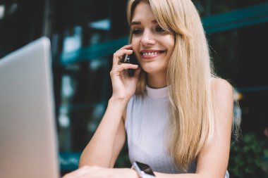 Açık kafede serbest iş yaparken akıllı telefon ve tarama modern laptop konuşurken büyüleyici gülümseme ile güzel genç kadın