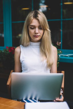Rahat açık kafede masada yakın oturan ve modern laptop serbest iş yaparken sarı saçlı odaklı genç kadın