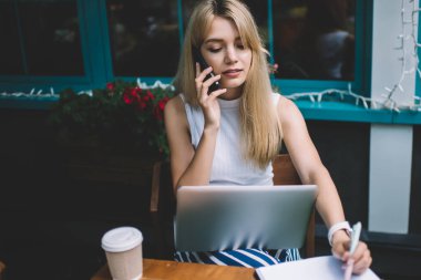 Şehir sokak açık kafede serbest iş yaparken laptop ile akıllı telefon konuşma ve Pano üzerinde notlar yapma sahip güzel genç bayan