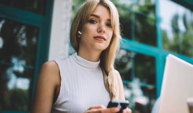 Şehir sokak açık kafede serbest iş yaparken sarı saçlı modern smartphone tarama ve kamera bakarak güzel kadın