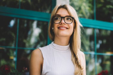 Sıcak içecek ve modern akıllı telefon fincan ile Pretty genç kadın gülümseyen ve açık kafede serbest iş yaparken uzak bakıyor