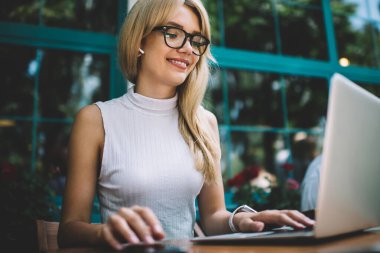 Şehir Caddesi üzerinde rahat açık kafede masada otururken şık gözlük gülümseyen ve modern dizüstü tarama güzel genç kadın