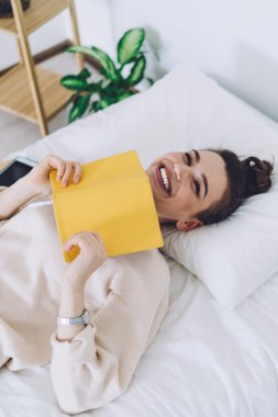 Ev elbiseleri içinde mutlu genç bir bayanın yatakta uzanıp günlük okumasından ve eğlenceli bölümlere gülmesinden.