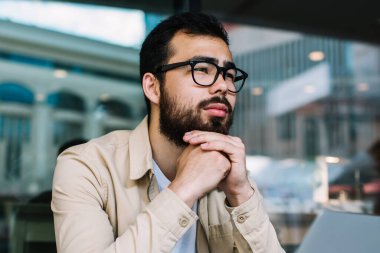 Gözlüklü düşünceli bir erkek programcı dizüstü bilgisayardaki veritabanının güncellenmesi üzerine kafa yoruyor kafeteryada elinde netbook ile oturmuş uygulamayla web sitesi oluşturma fikri üzerinde düşünüyor.