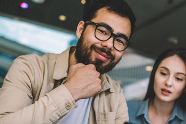 Gözlüklü neşeli sakallı hippi adamın portresi kameraya gülümsüyor ve güzel beyaz kız arkadaşıyla vakit geçirmekten zevk alıyor yanında oturuyor ve cep telefonunun ekranına bakıyor.