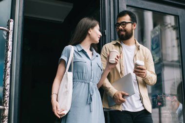 Kafeteryadan ellerinde kafein içecekleriyle çıkan ve zevk içecekleri hakkında iletişim kuran çeşitli çiftler. Hafta sonları gezmek için fikir alışverişinde bulunan mutlu erkek ve kadın hipsterler.