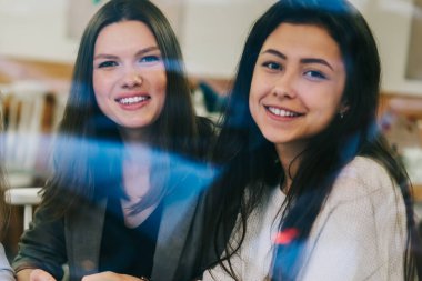 Neşeli kadın partnerlerin portresi, tanıtım alanında elinde modern aletlerle oturan ve işbirliği sırasında gülümseyen, teknoloji kullanan mutlu kadınların portresi.