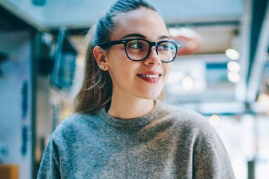 Elinde cep telefonu olan neşeli bir kadın blog yazarı kafenin içinde boş zamanlarında gülümsüyor ve başka tarafa bakıyor. Kafeteryada günlük giysiler giyen mutlu bir yeniyetme kız.