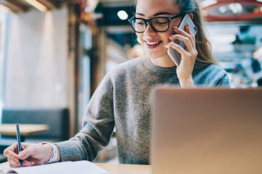 Online danışmanlık için müşteri hizmetlerini arayan olumlu kadın akıllı telefon konuşmaları sırasında ders kitabına not alan dizüstü bilgisayar aygıtı için yaklaşık 4G internet bağlantısı, gençlik yaşam tarzı kavramı