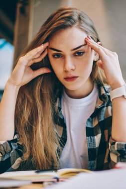 Fotoğraf makinesine bakan yorgun kız öğrencinin portresi ve eğitim için edebiyat kitaplarıyla sınav hazırlıkları sırasında kendini bitkin hisseden, tanıtım alanında baş ağrısı çeken yorgun hippi kız.