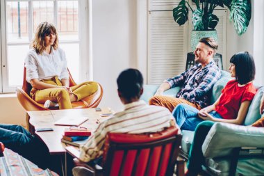 Masanın etrafında rahat koltuklarda oturan ve şık oturma odasında birbirleriyle iletişim kuran bir grup rahat insan.
