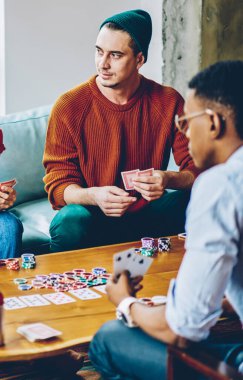 Masanın etrafında poker oynarken ve evde birlikte harika vakit geçirirken içki içerken çok ırklı, yoğun bir takım elinde kart tutuyor.
