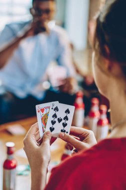 Kırmızı tişört giyen, elinde kartlarla çok ırklı arkadaşlarıyla poker oynayan ve modern apartmandaki içeceklerle masada oturan mahsul kadınların arka planı.