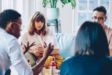 Rahat bir oturma odasında parti için toplanan şişelerle masada oturan sıradan giyinmiş bir grup zeki genç.