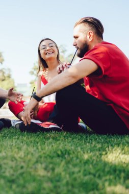 Günlük giysiler içinde bir grup genç soğuk içeceklerin tadını çıkarıyor ve güneşli bir yaz günü parkta çimlerde otururken birbirleriyle sohbet ediyorlar.