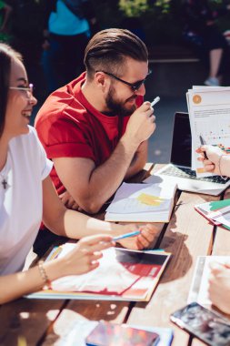Bir grup genç arkadaş, açık kafede oturup ödev yaparken verilerle gülümsüyor ve kağıtları tartışıyor. Açık havada öğrenim görürken beyin fırtınası yapan dört öğrenci.