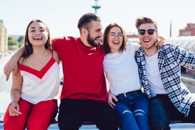 Güneşli bir günde, şehir caddesinde yürüyüş sırasında sınırda otururken neşeyle gülüp kucaklaşan bir grup genç. Mutlu gülümseyen dört arkadaş gençliğin ve yaz gününün tadını çıkarıyor.