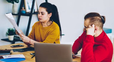 Erkek ve bayan meslektaşlar proje kontrol bildirimi ve bilgilerini birlikte masaya oturtmada danışmanlık yapıyorlar. Düşünceli bir adam ev içi sınavlar için bayan öğrencilere bakıyor.