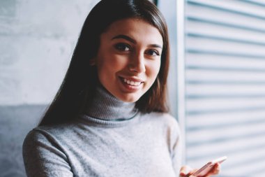Fotoğraf makinesi bakıyor ve gülümseyen, milenyal hipster kız bloglama için gadget 'ları kullanarak dizüstü bilgisayar üzerinde web deposunda işlem yapmak için smartphonekullanarak başarılı kaygısız kadın Blogger portresi